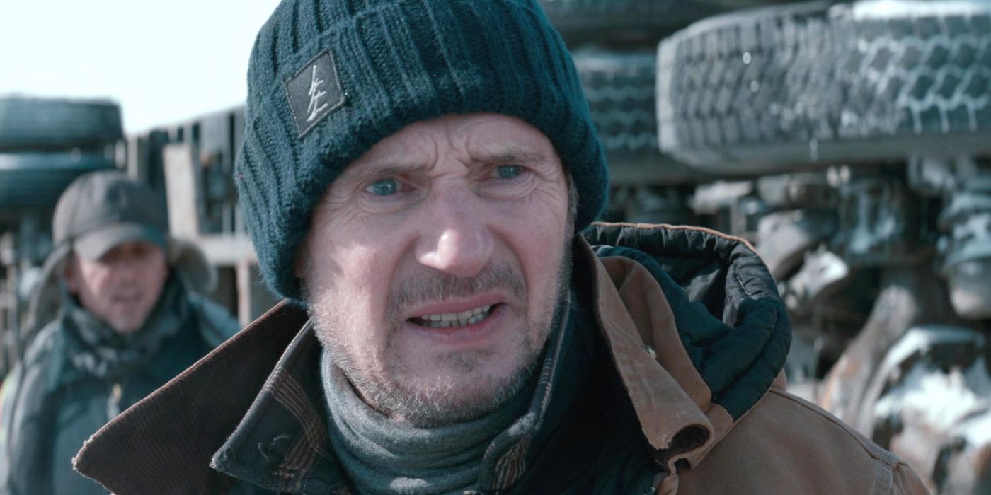 Liam Neeson as Mike McCann in The Ice Road grimacing intensely in the cold with a crashed truck behind him