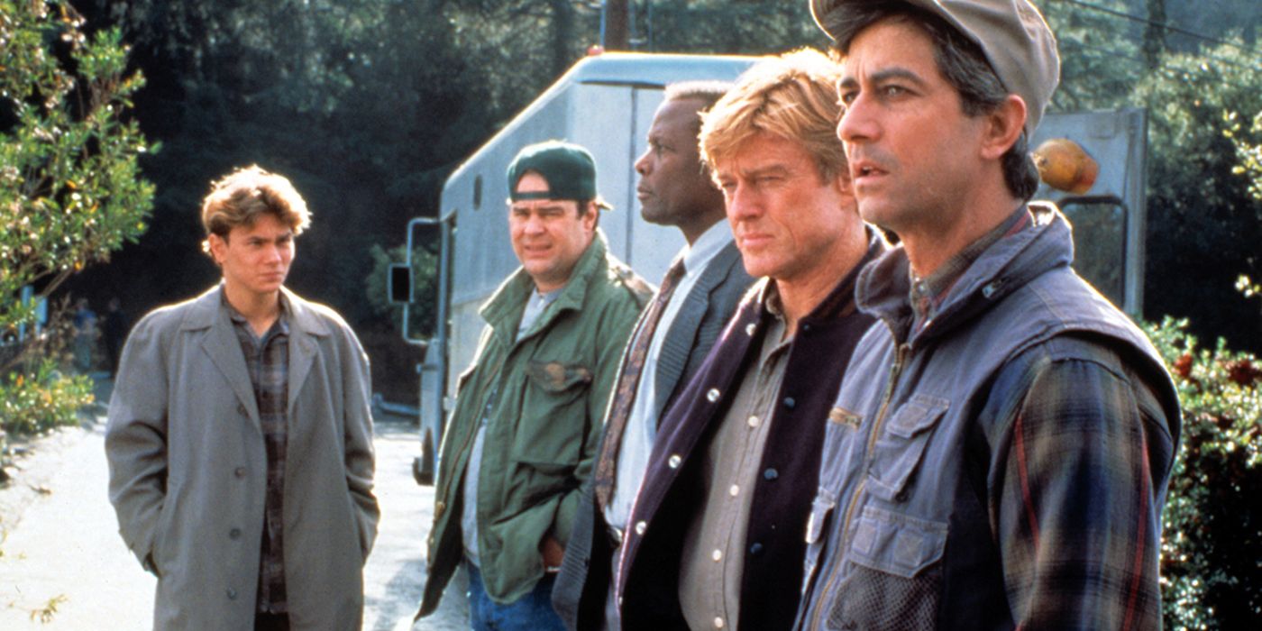 River Phoenix, Dan Aykroyd, Sidney Poitier, Robert Redford, and David Strathairn in Sneakers are stood as their characters looking pensive in an outdoor setting.