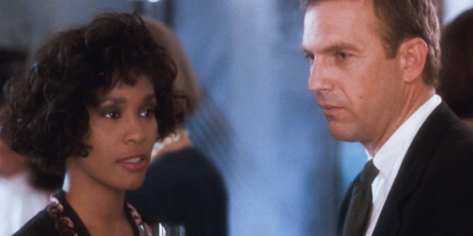 Whitney Houston como Rachel e Kevin Costner como Frank olhando para coisas diferentes no Guarda-Costas