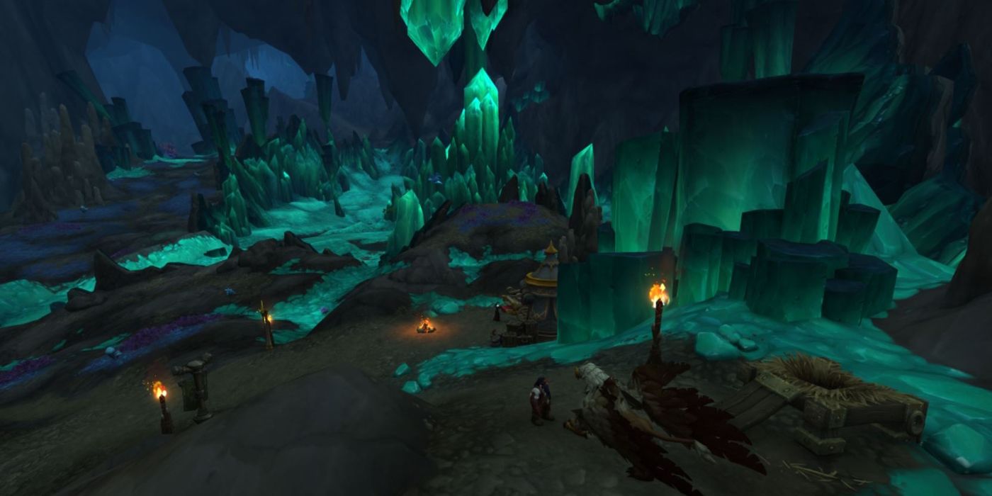 WoW Zaralek Caverns Zone, area di dalam gua bawah tanah dengan pilar hijau bercahaya yang keluar dari tanah dan langit-langit.
