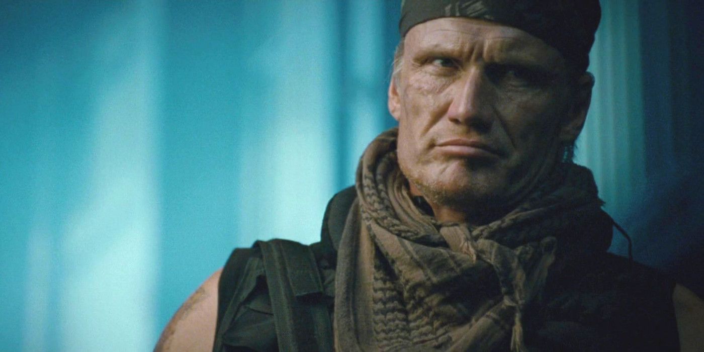 Dolph Lundgren In The Expendables 2 frowning in a neck scarf and backward baseball cap