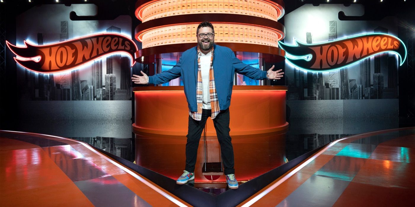 The host of Hot Wheels Ultimate Challenge stands on a brightly lit stage