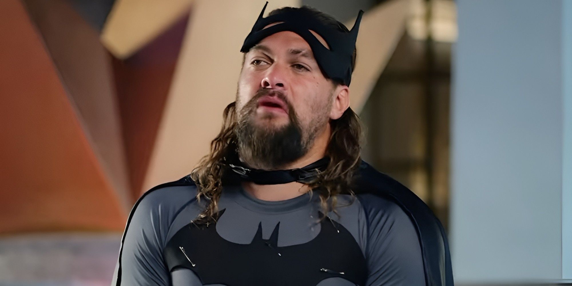 Jason Momoa sitting while dressed up as Batman for a theme park commercial.