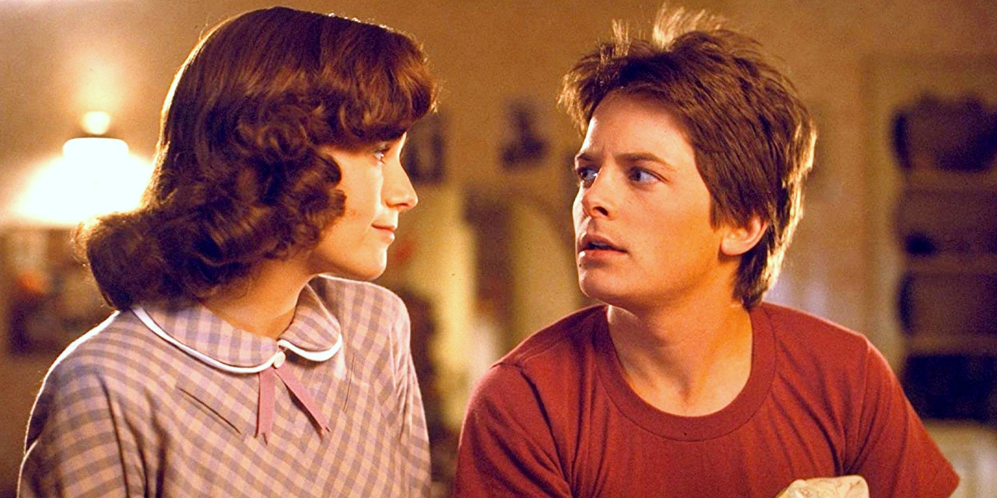 Lea Thompson and Michael J Fox in Back to the Future sitting on a bed and looking at each other in Back to the Future