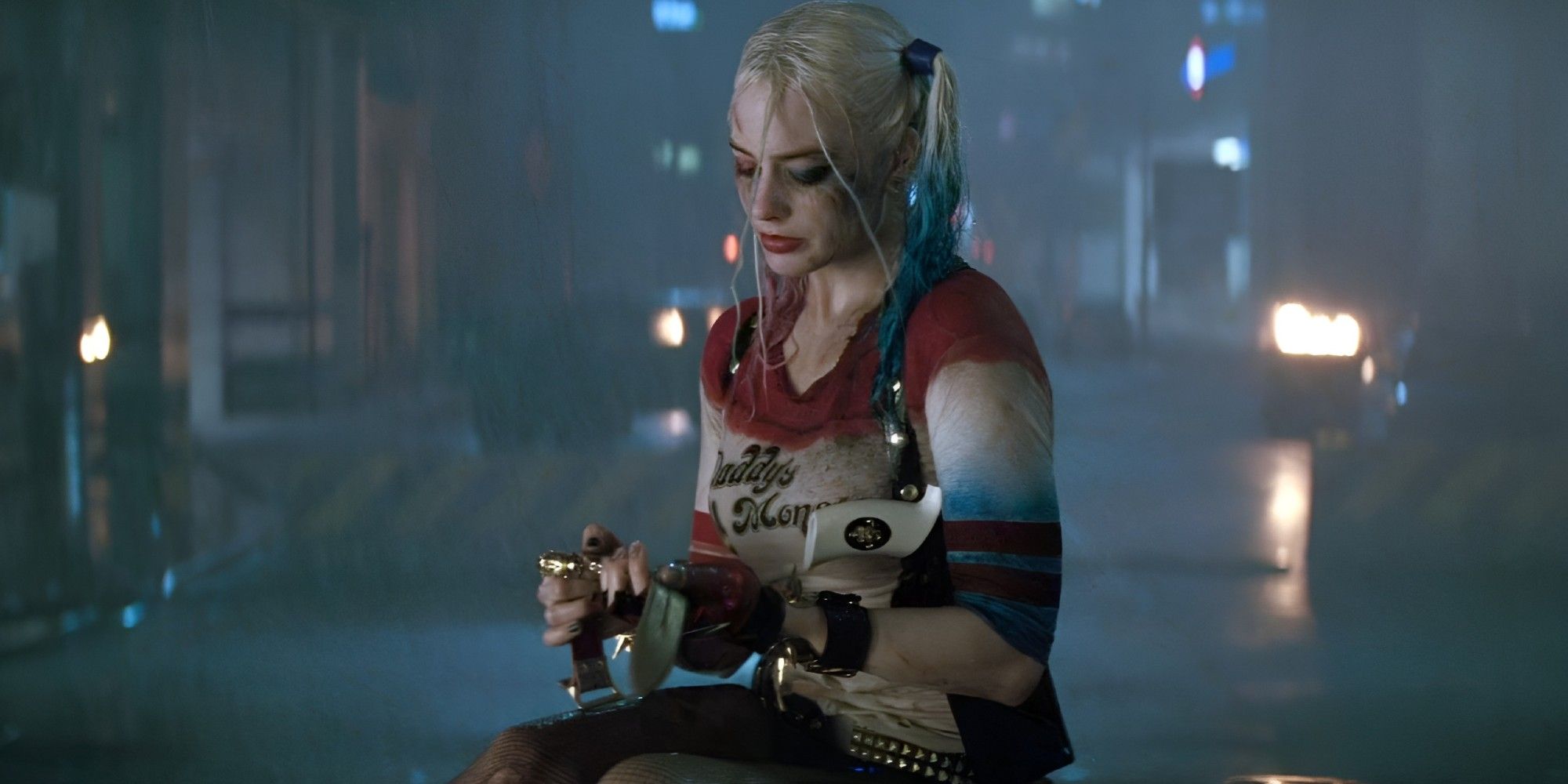Margot Robbie as Harley Quinn sitting down in the middle of a street while it rains in a scene from 2016's Suicide Squad