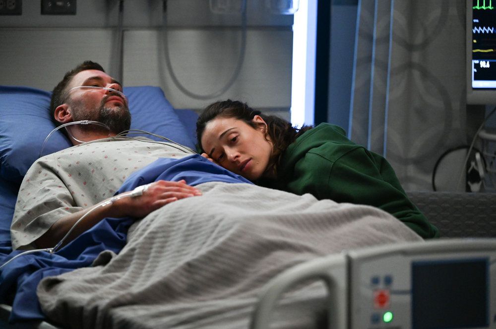 Ruzek in the hospital bed as a woman lays over him