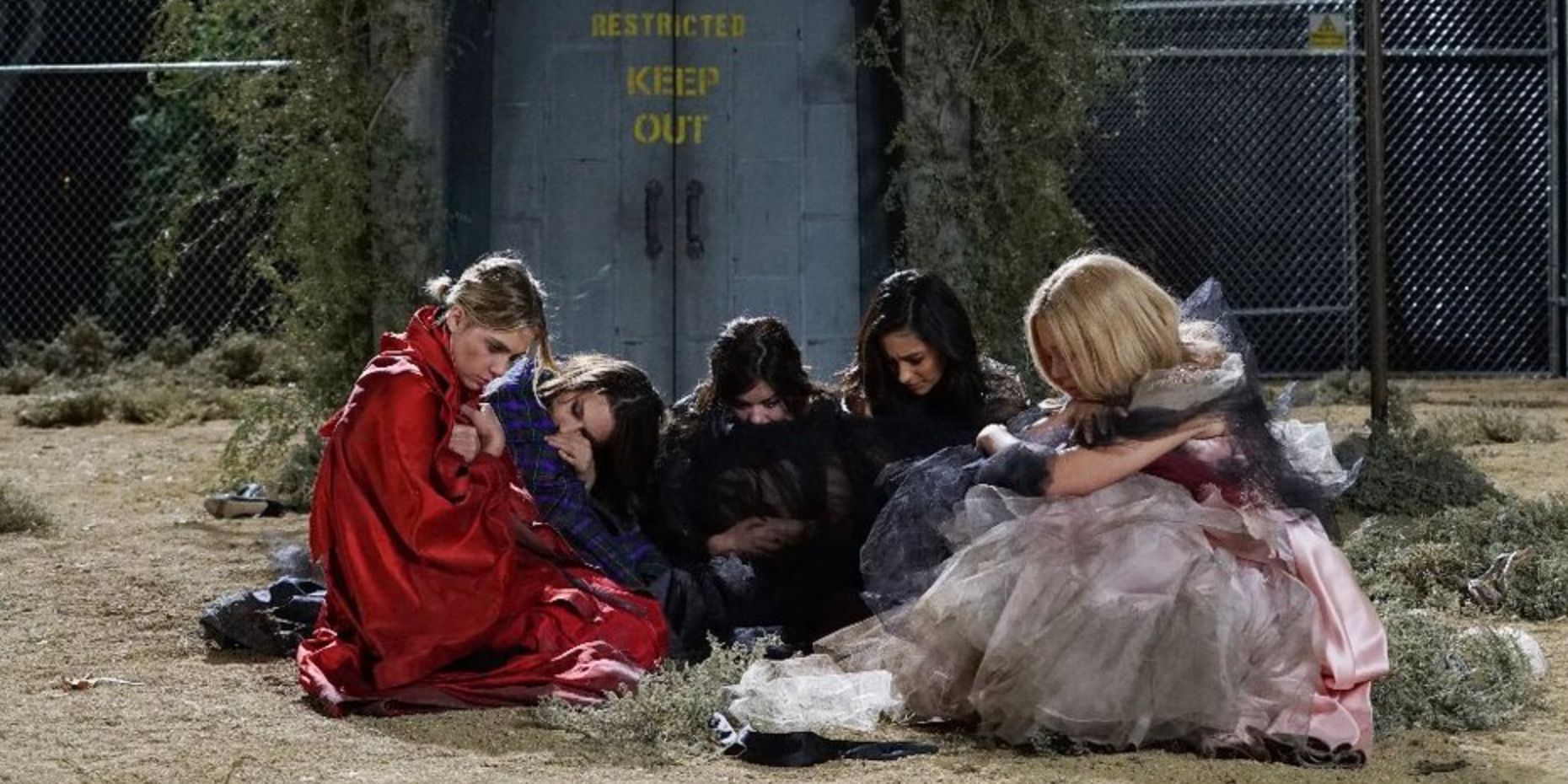 The Liars and Mona outside of the dollhouse huddled together in disheveled dresses in Pretty Little Liars