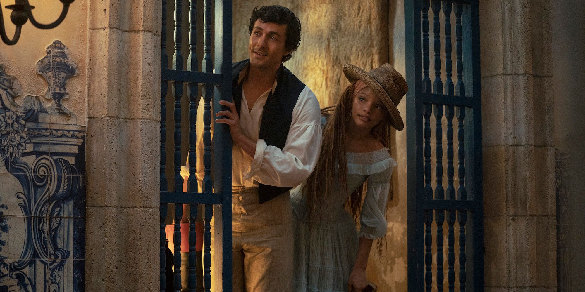 Eric and Ariel peeking around a gate in The Little Mermaid (2023)