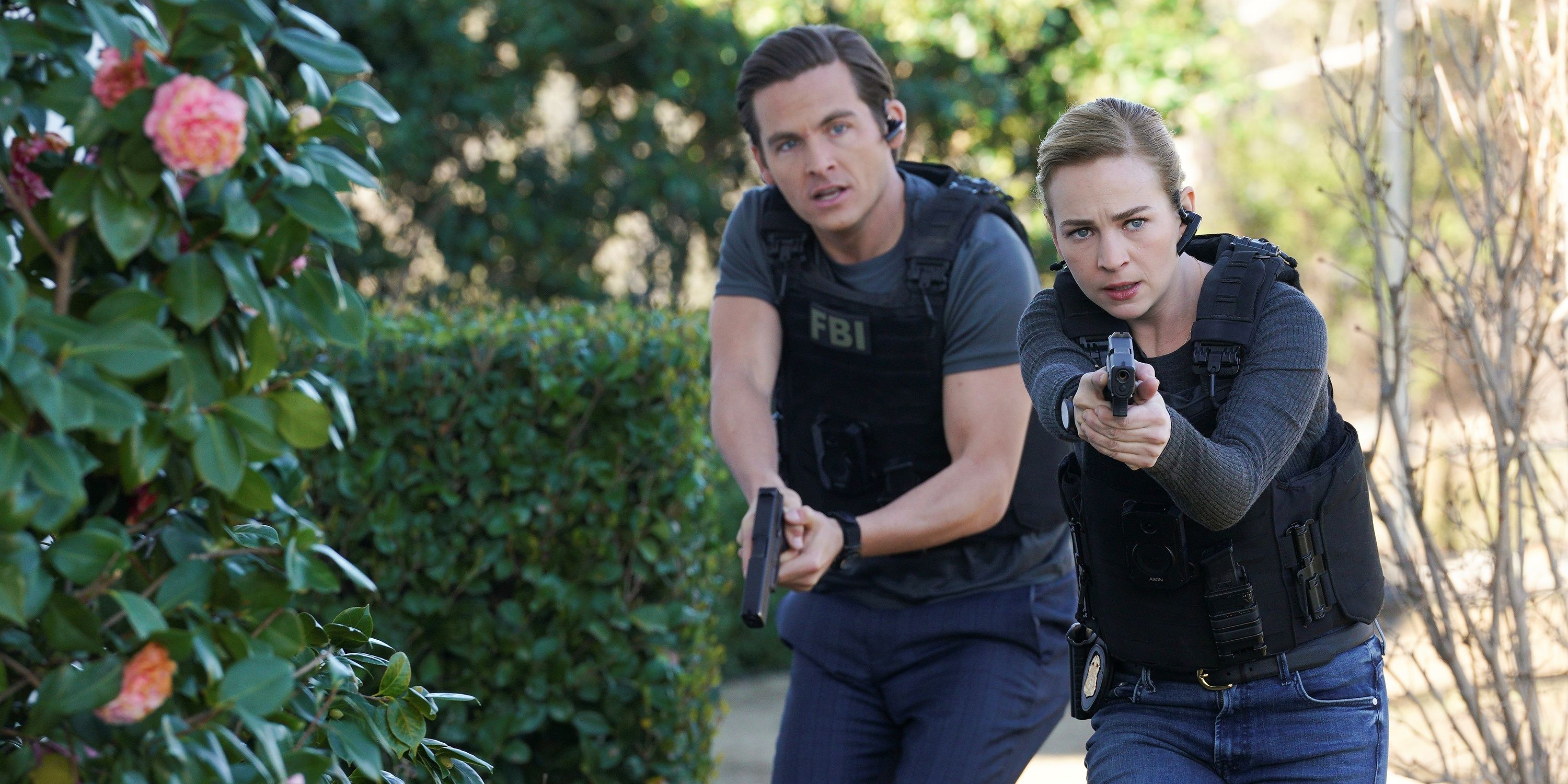 Laura and Brendon track down a suspect in The Rookie: Feds season 1. Laura wears a black bullet proof vest over a dark gray long-sleeved shirt and jeans. Brendon wears a black bullet proof vest over a dark gray shirt and jeans.