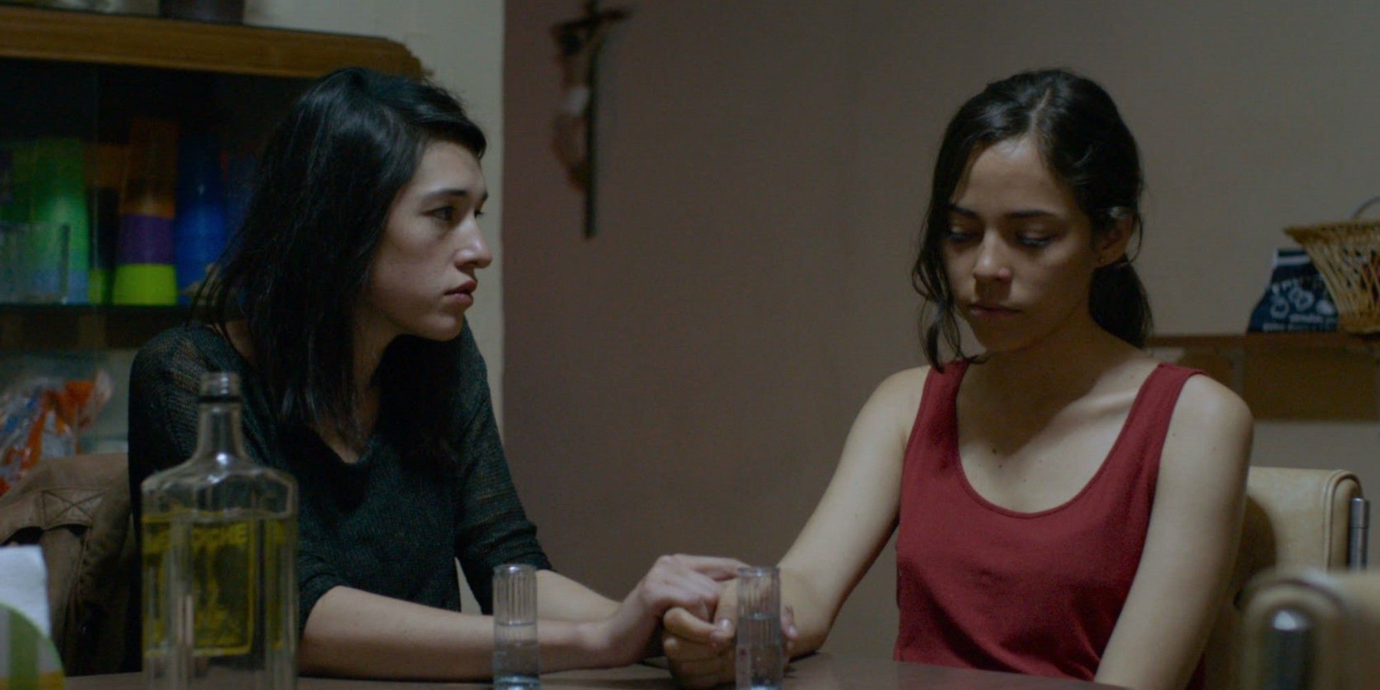 Alejandra and Verónica holding hands at a kitchen table in The Untamed.