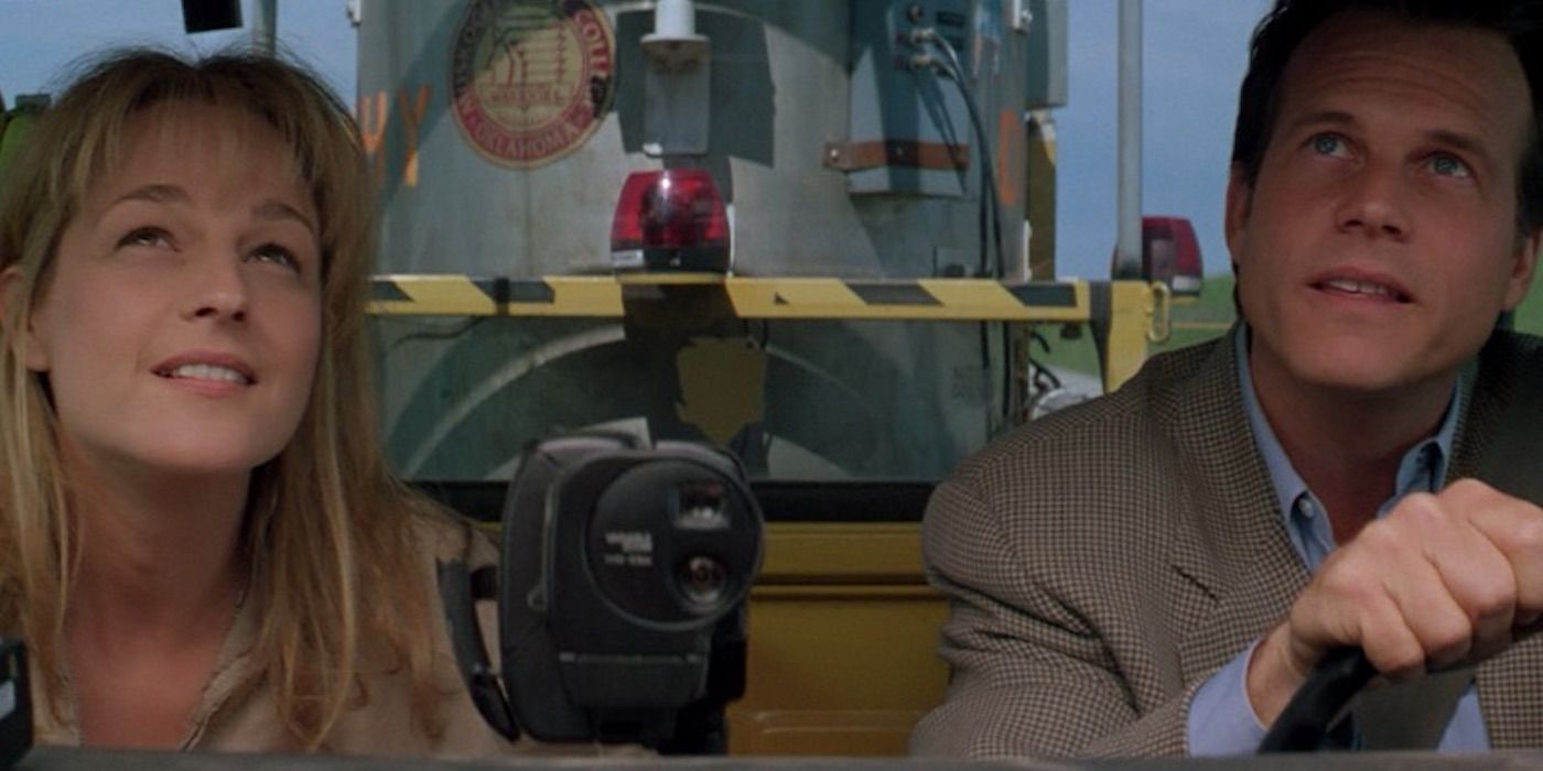Bill Paxton driving a truck with Helen Hunt in the passenger seat as a large container is visible behind them in Twister.