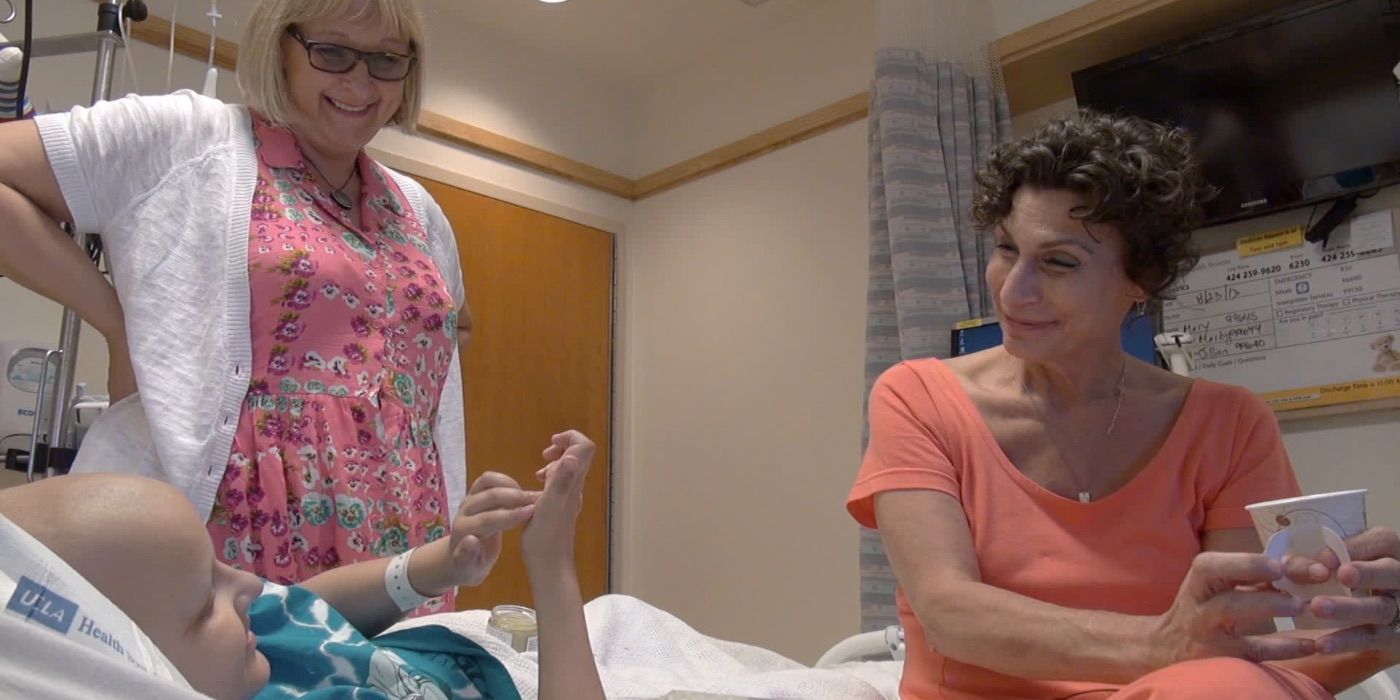 Two women talk to a child in a hospital bed in Weed the People
