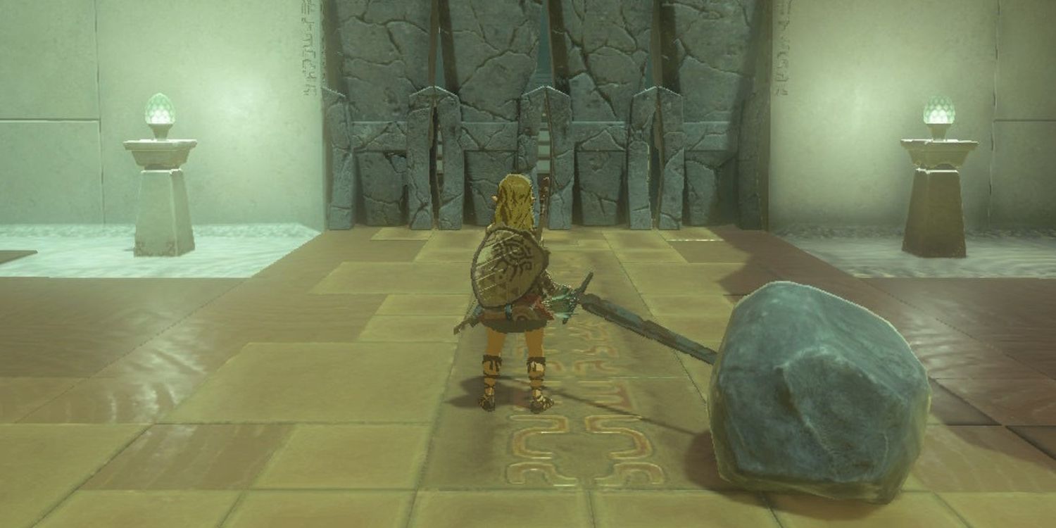 Link stands before a cracked, rocky wall holding a giant hammer in Tears of the Kingdom. The hammer is comprised of a giant boulder fused to a rusty sword.