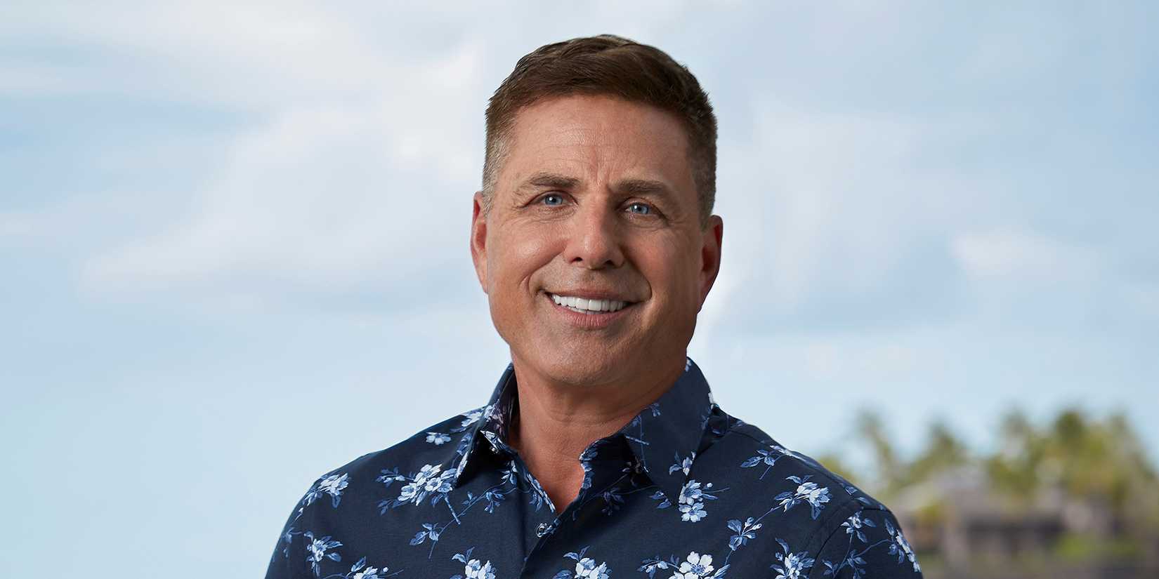 Host Mark L Walberg from Temptation Island smiling outside on island