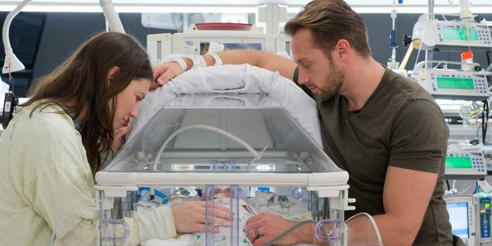 Adam and Danielle Busby in the hospital looking down at one of their quints in an incubator.