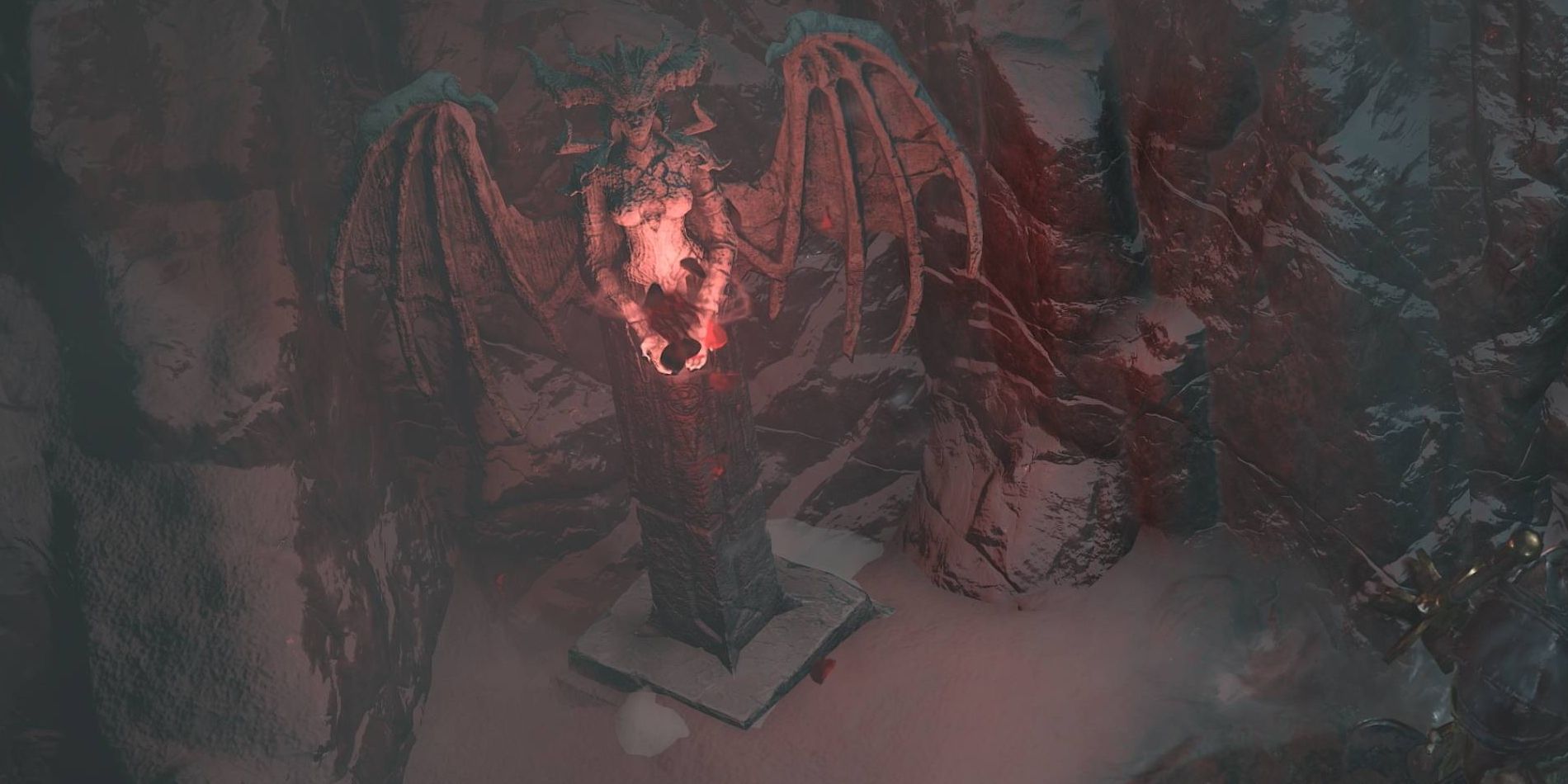 Une statue de l'antagoniste cornue et ailée Lilith rougeoyante dans une niche rocheuse couverte de neige.