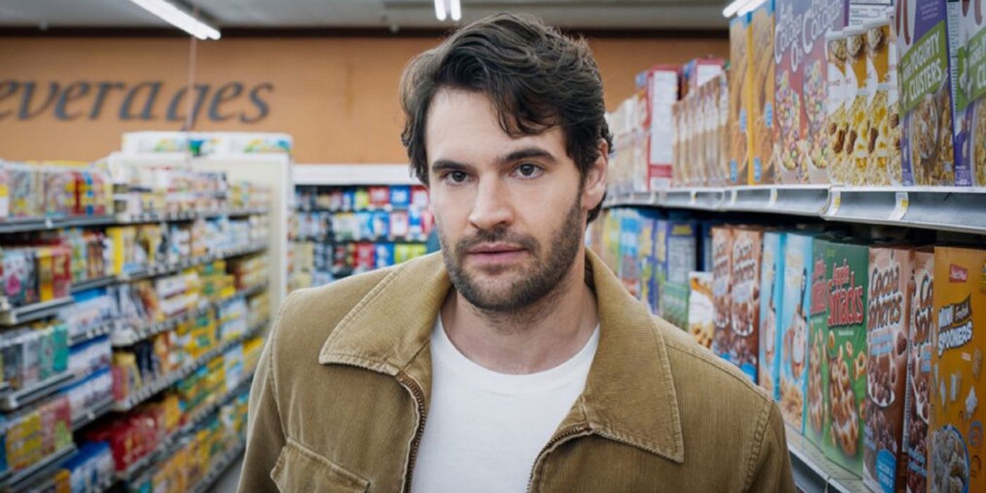 Tom Bateman stands in a cereal aisle with a serious expression on his face.