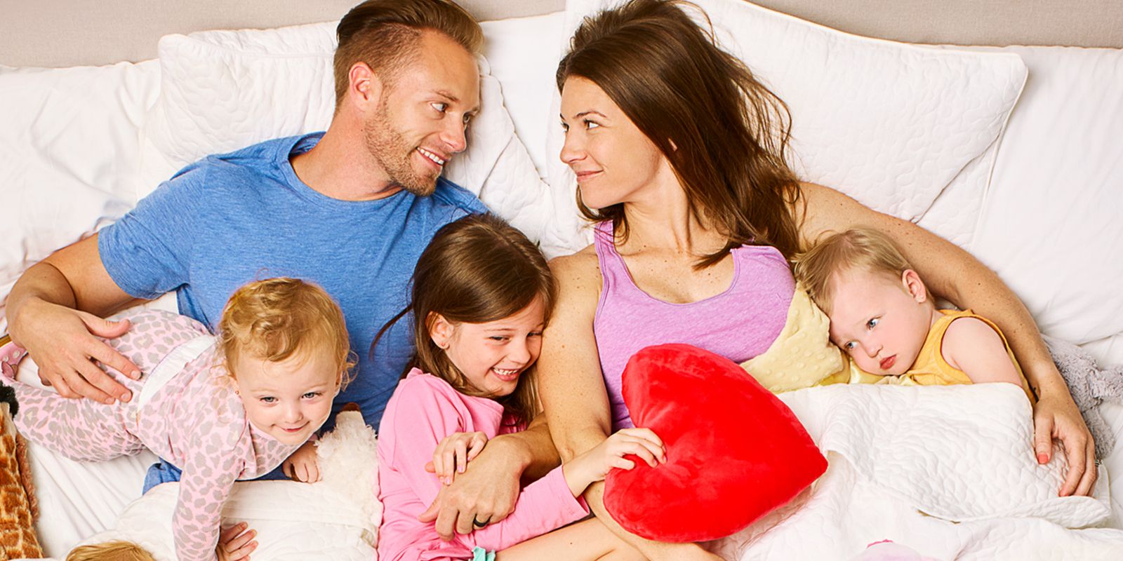 Danielle and Adam Busby laying down in bed looking at one another with their children