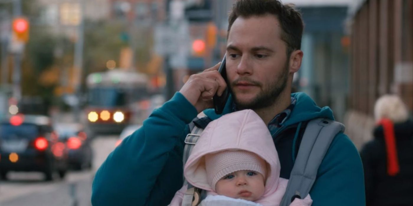 Ian al teléfono mientras carga a un bebé en la calle en Workin' Moms