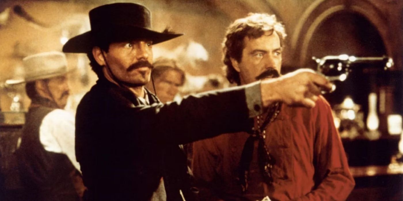 Johnny Ringo aiming a gun in a saloon as Curly Bill watches in Tombstone