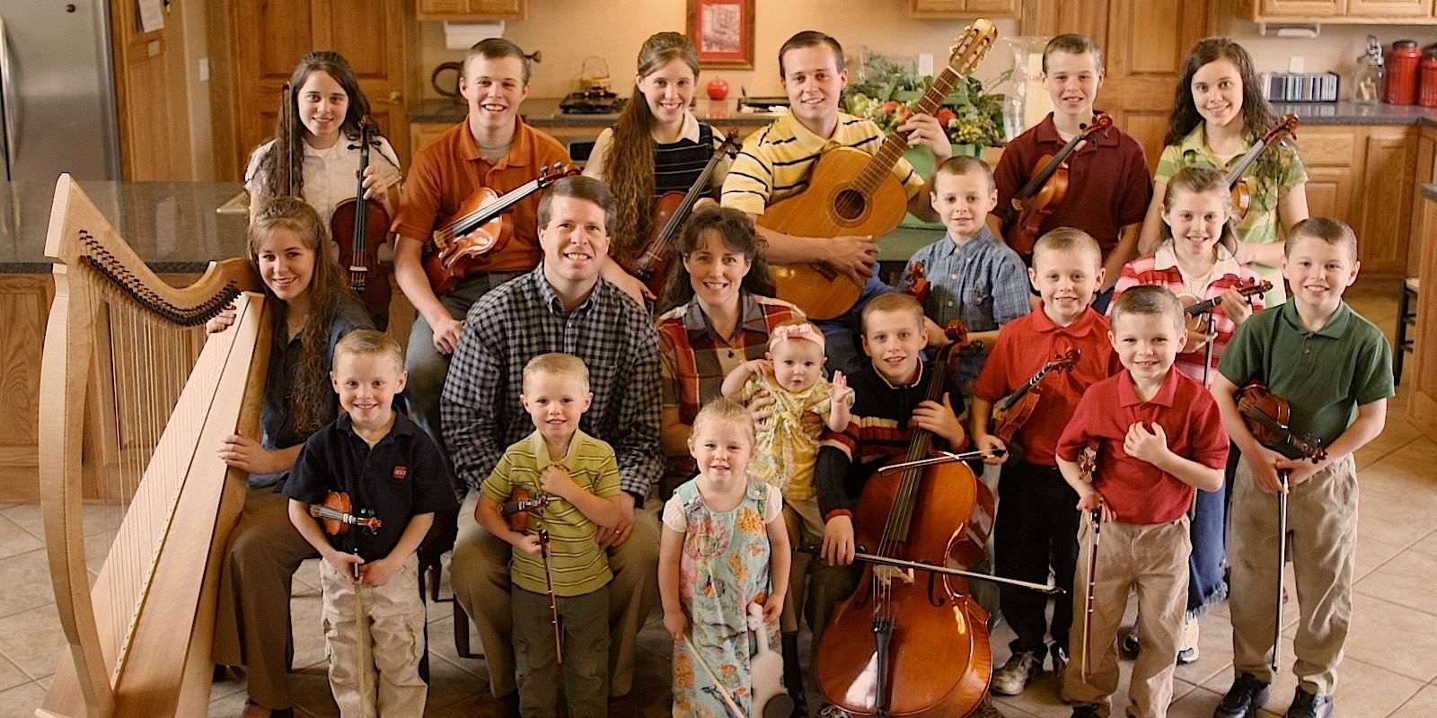 19 Kids and Counting's Duggar Family standing next to each other in their kitchen holding their instruments and smiling at the camera
