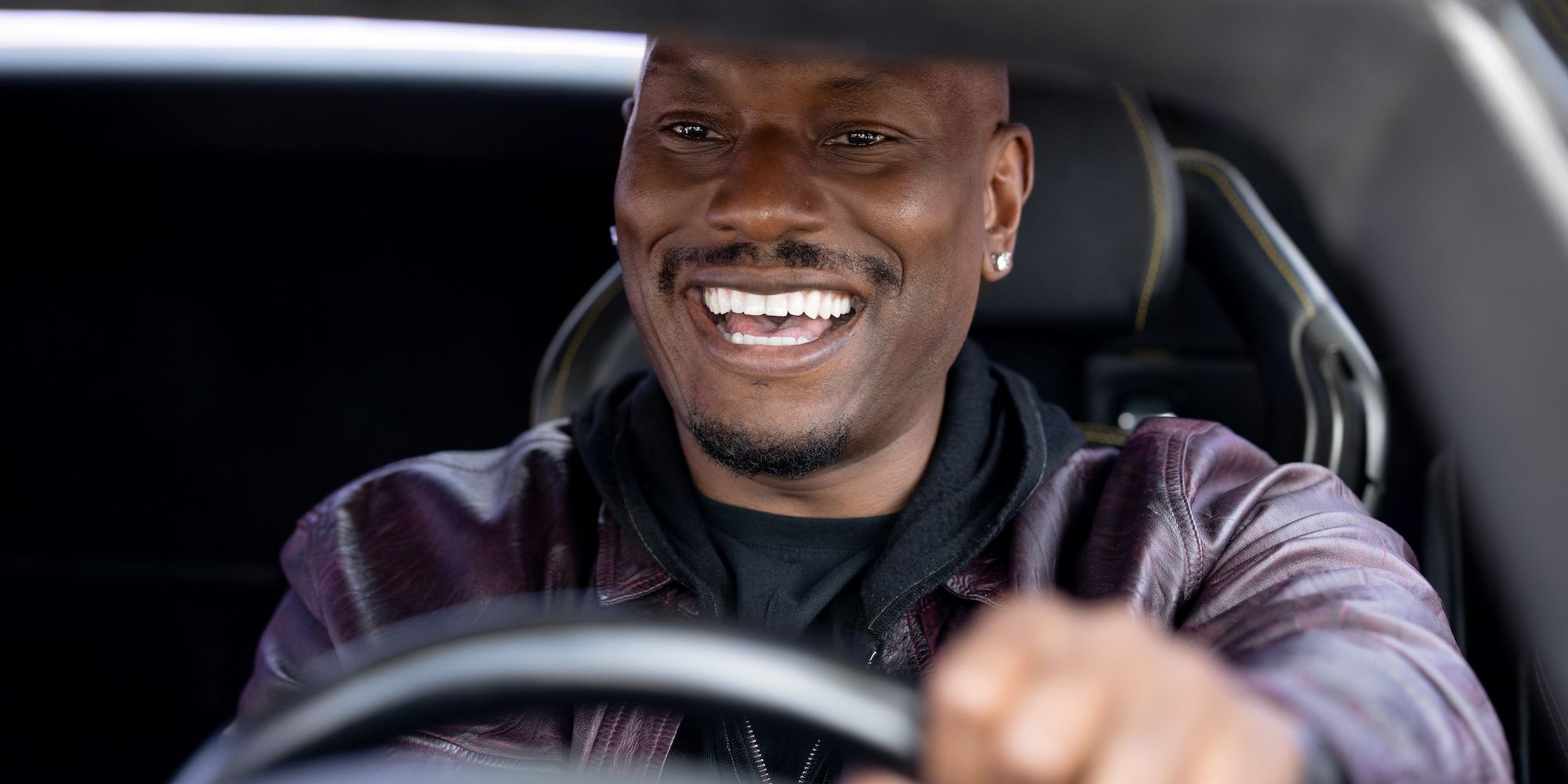 Roman (Tyrese Gibson) driving a car and smiling in the Fast & Furious franchise