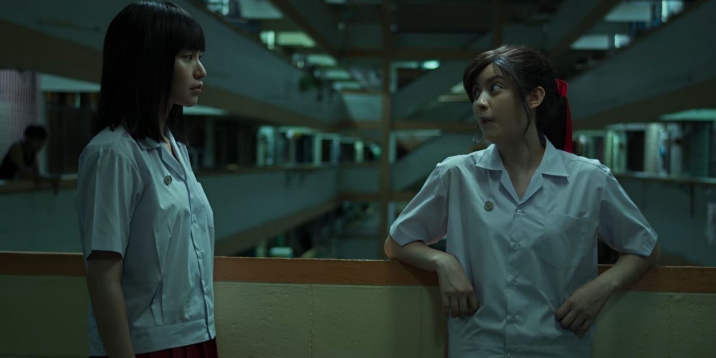 Two girls talk to one another in a school. 