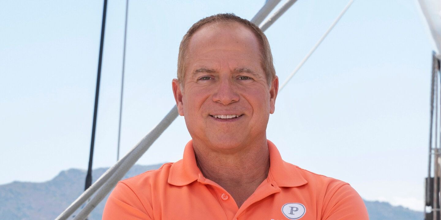 Captain Glenn Below Deck Sailing Yacht wearing orange polo shit smiling on deck