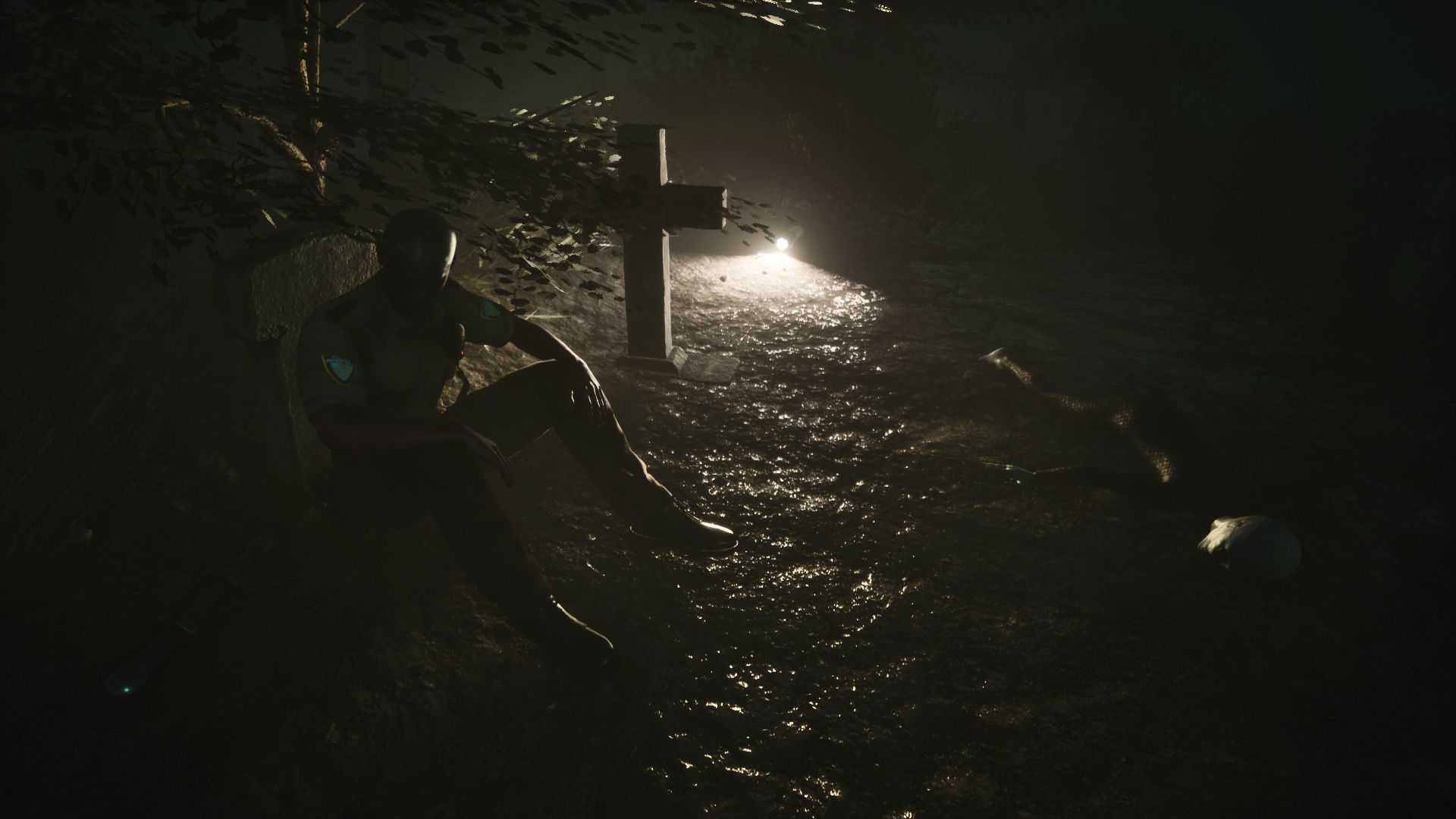Screenshot of Greyhill Incident shows cop sitting next to a grave and a dead Grey alien. A flashlight acts as a small light source amongst the dark environment.