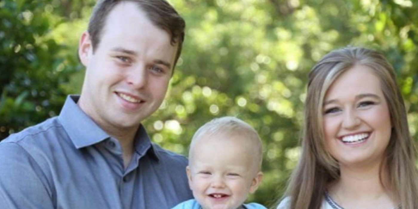 Joseph Duggar smiling holding his son and standing next to his wife 