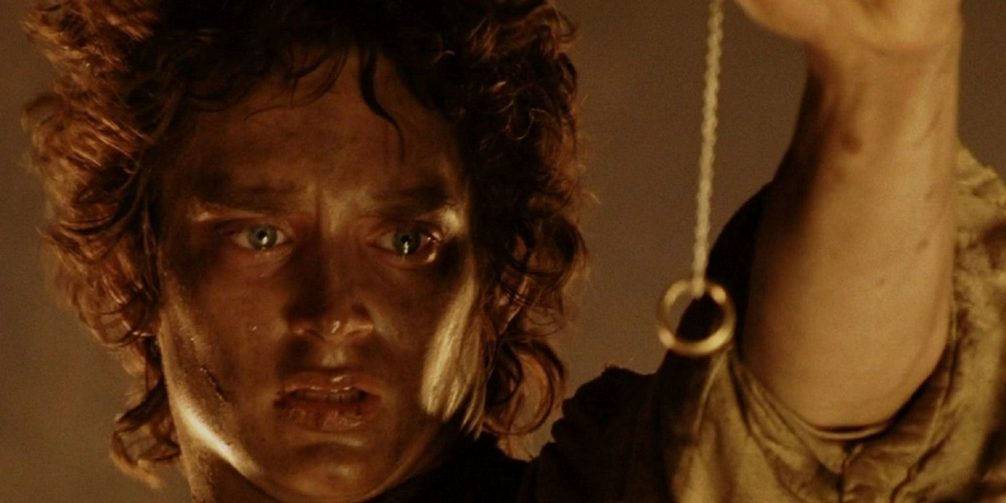 Elijah Wood covered in dirt and soot as Frodo, gazing longingly at the One Ring.