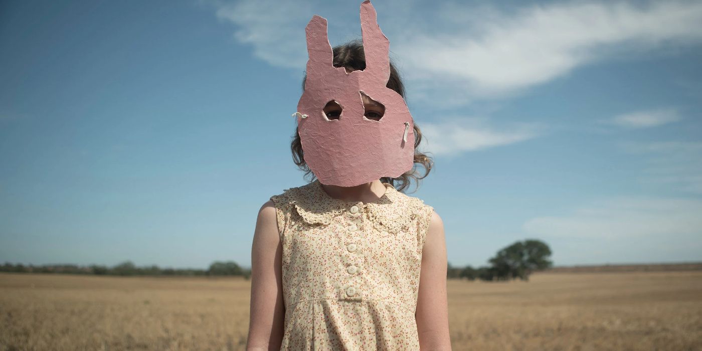 Mia stands in a field wearing a pink cutout bunny mask.
