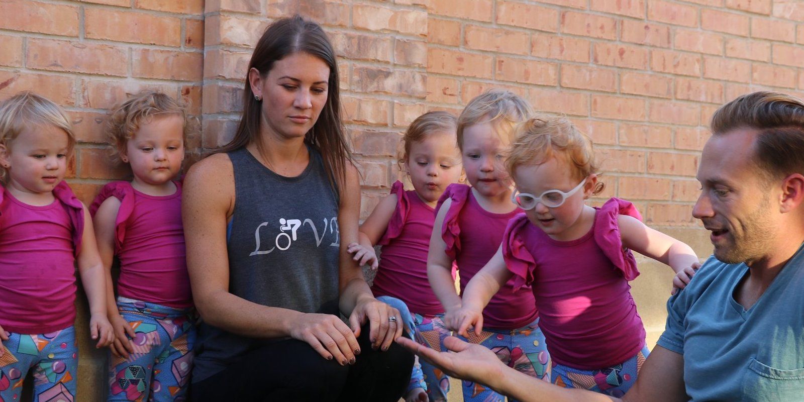 Danielle Busby sitting next to the quintuplets with Adam Busby in front of her reaching out his hand.