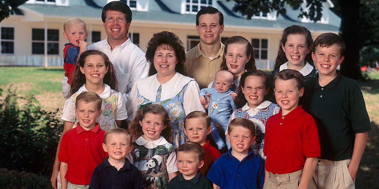 The Duggar Family all standing together smiling for a picture in front of their house