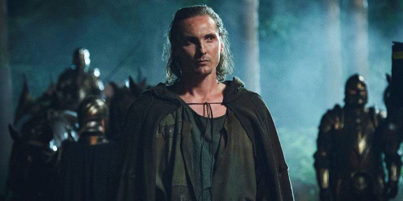 Eamon Farren as Cahir stood in a dark woodland in The Witcher season 3.