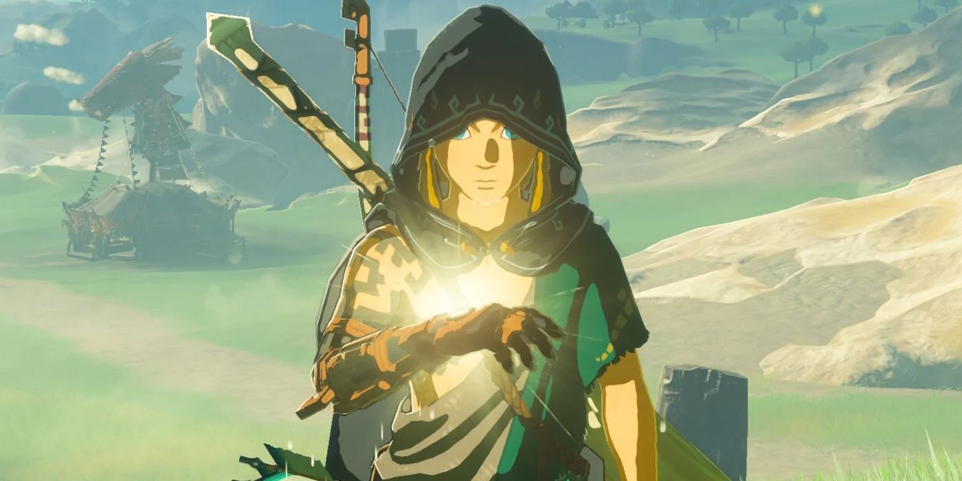 A screenshot from Tears of the Kingdom. A hooded Link stands in a field near a stable, looking down at a yellow glow emanating from the back of his hand. 