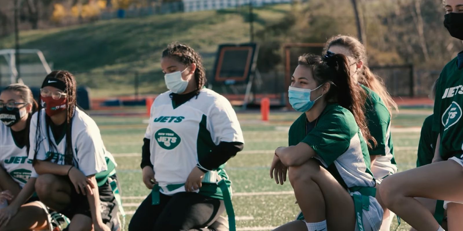 Football players take a knee while listening to the coach in the flag football docuseries EmpowHER.