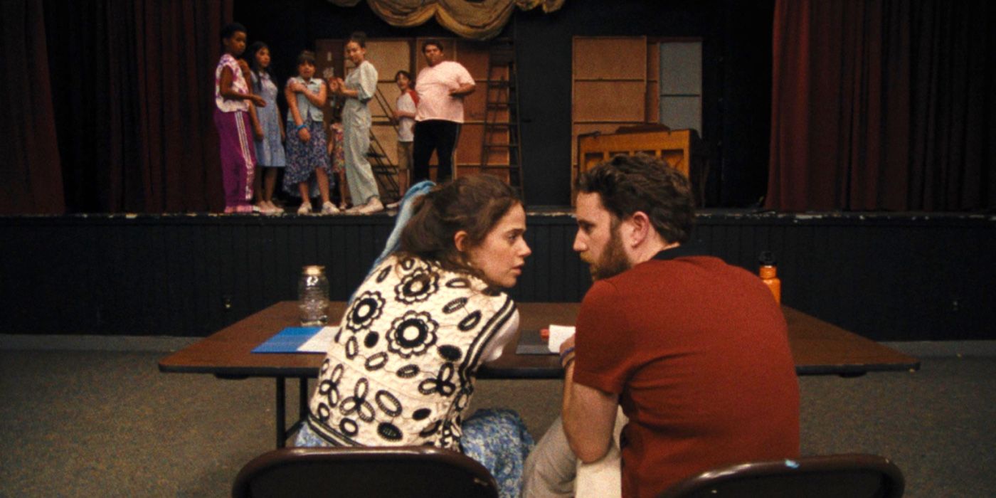 Theater Camp: Angelo and Rebecca talking at a table about the kids on stage 