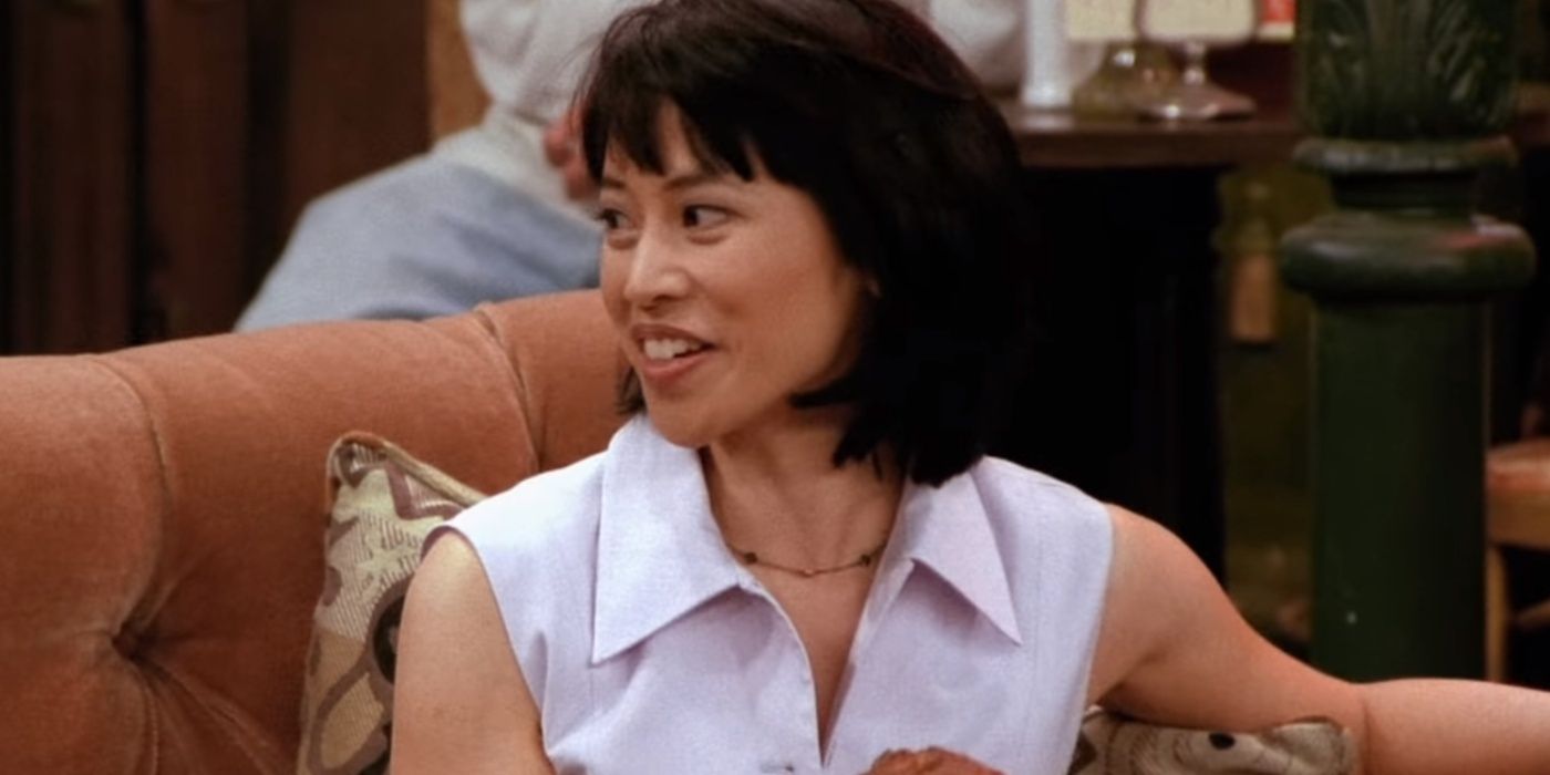 Julie holds a muffin and looks to her right at Central Perk in Friends