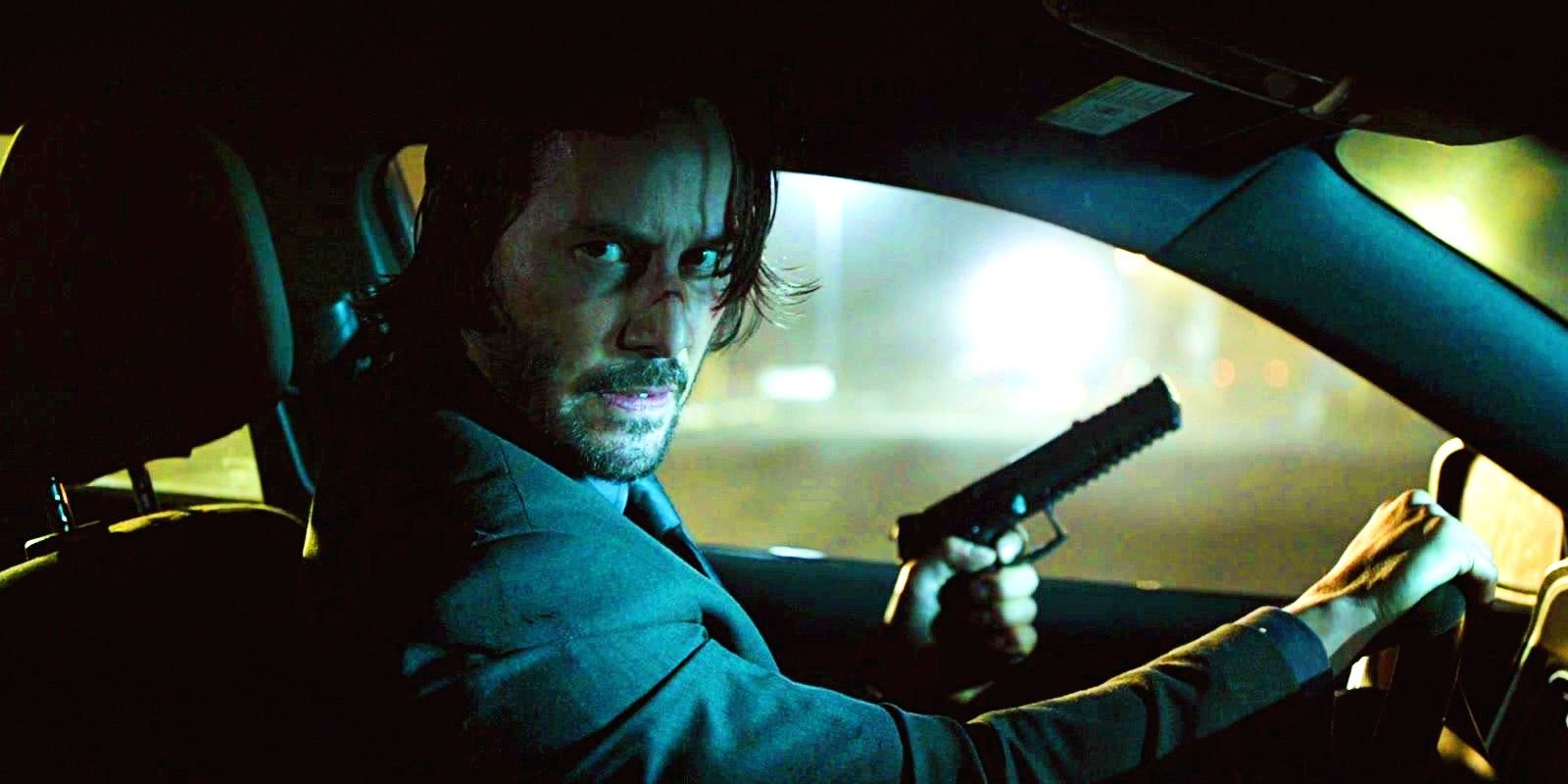 Keanu Reeves driving a car with a gun in hand in John Wick 4