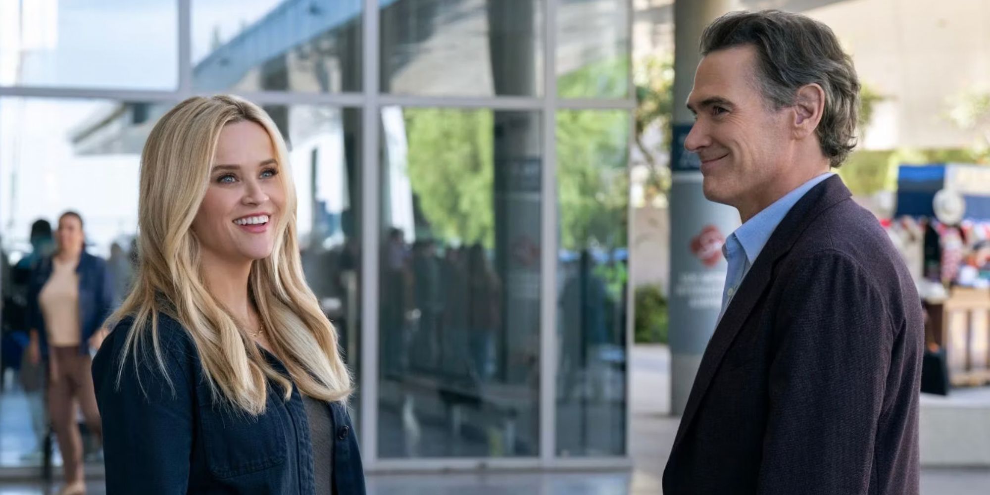 Reese Witherspoon and Billy Crudup smiling outside a building in The Morning Show