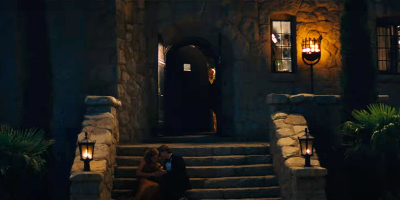 A man walks out the front door of the party, and two people kiss on the stairs.