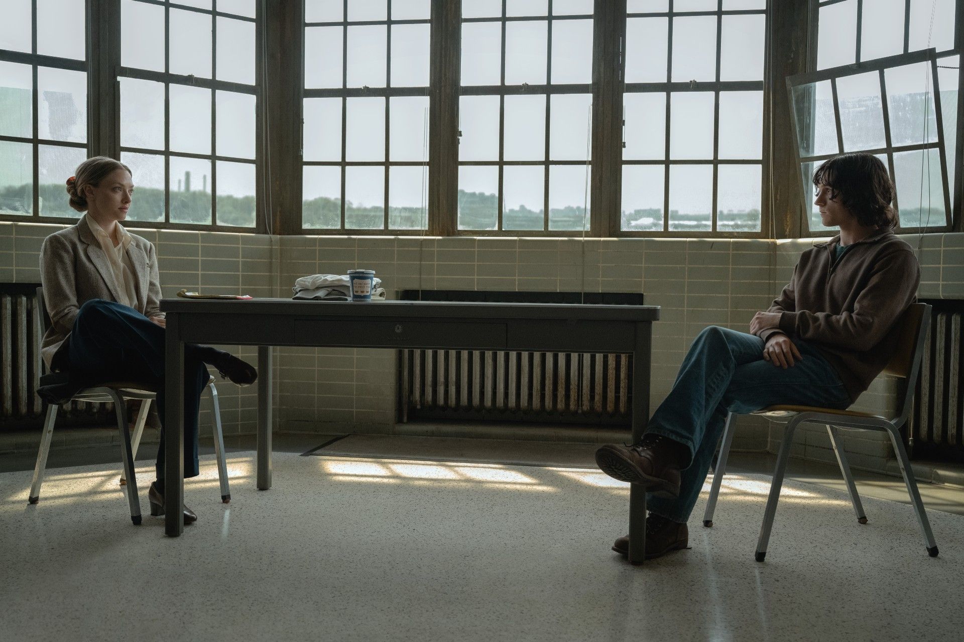 Amanda Seyfried and Tom Holland sitting across from each other in The Crowded Room during an interrogation.