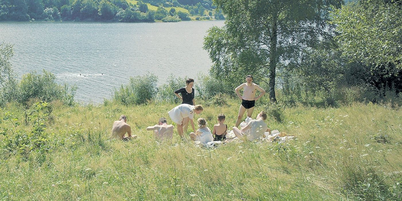 A still of the cast of The Zone of Interest in the grass by a lake.