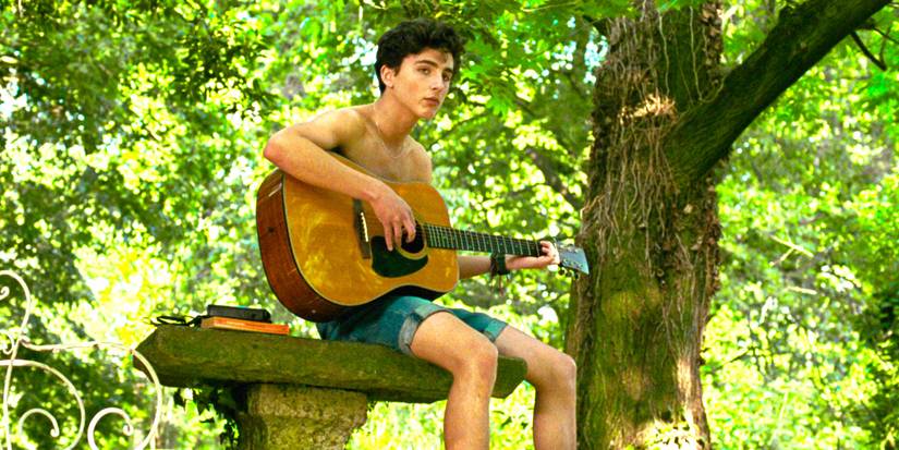  Timothee Chalamet in Call Me By Your Name sitting atop a stone table holding a guitar