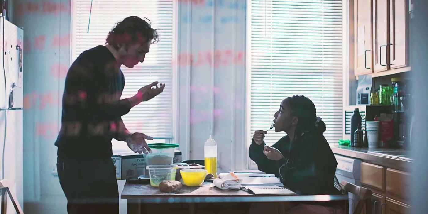 A screenshot from The Bear of Carmy and Sydney in the kitchen. Carmy is standing and gesturing with his hands, while Sydney is sitting and has a spoon in her mouth.