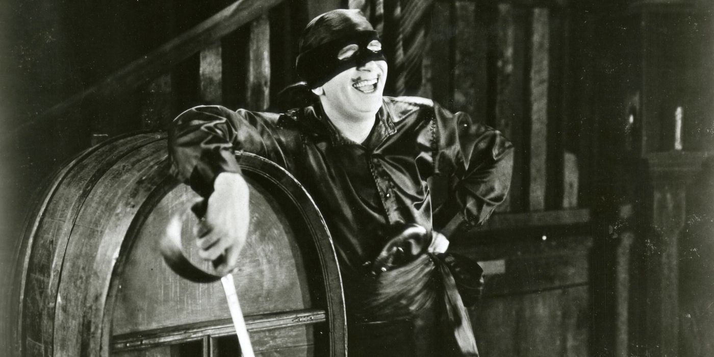 Douglas Fairbanks laughing while leaning against a barrell and holding a sword in The Mark of Zorro