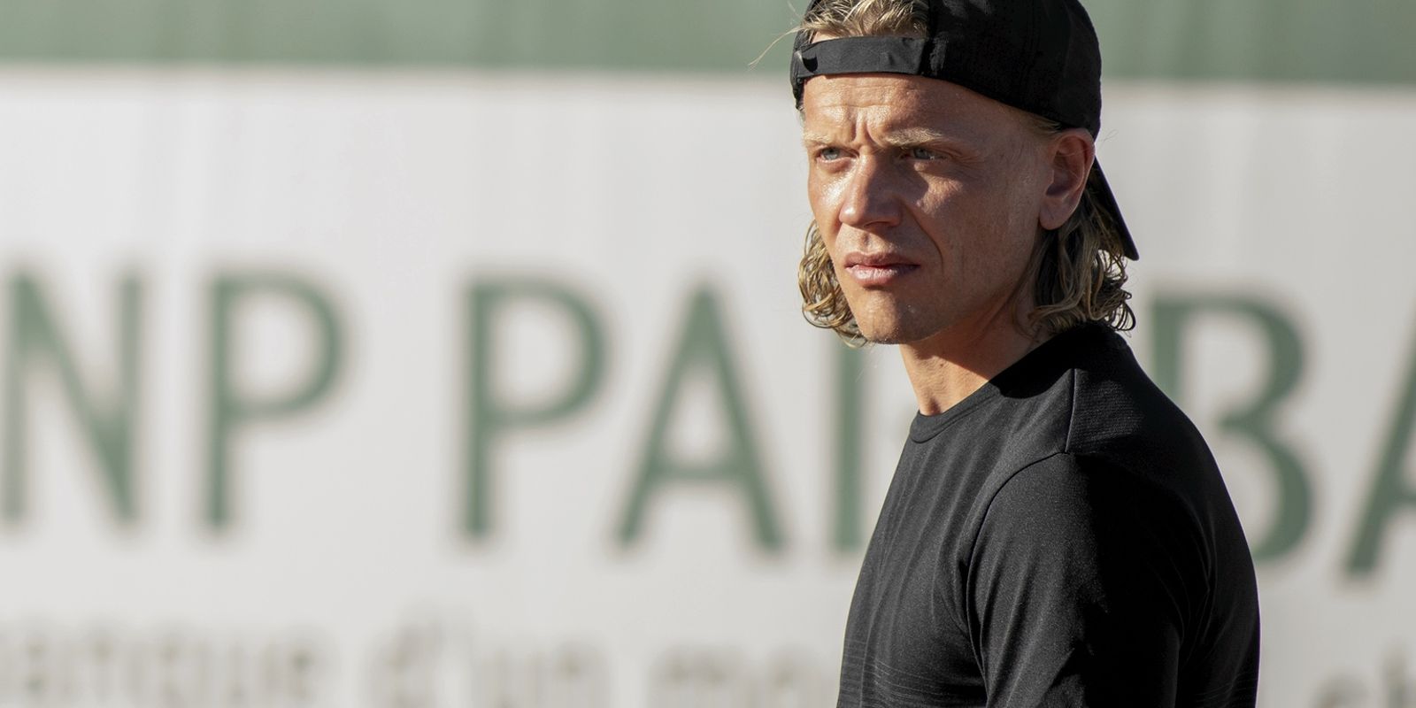 Thomas stands on the tennis court wearing a backwards baseball hat.