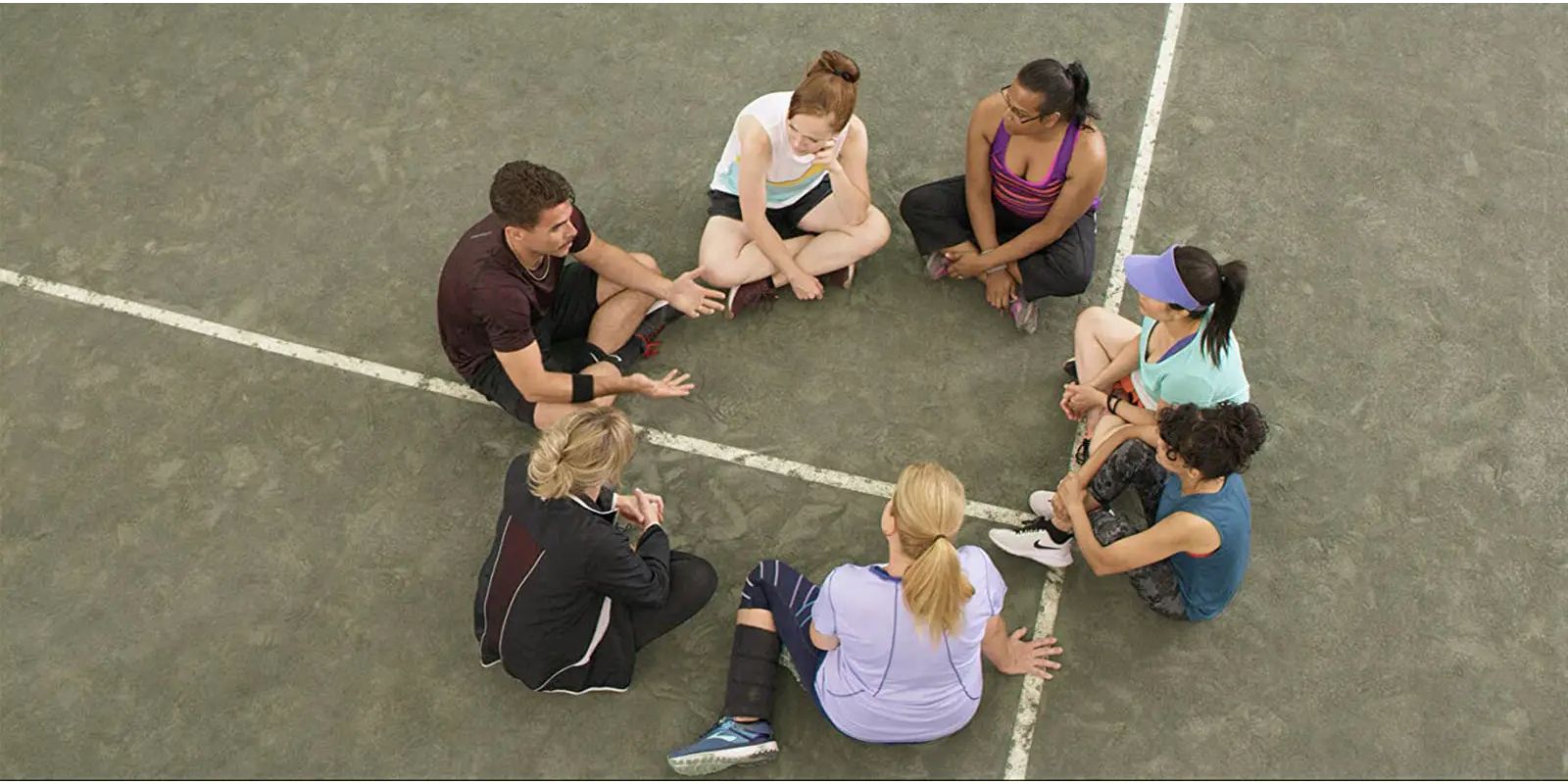 The tennis team sits together on the court in First One In.