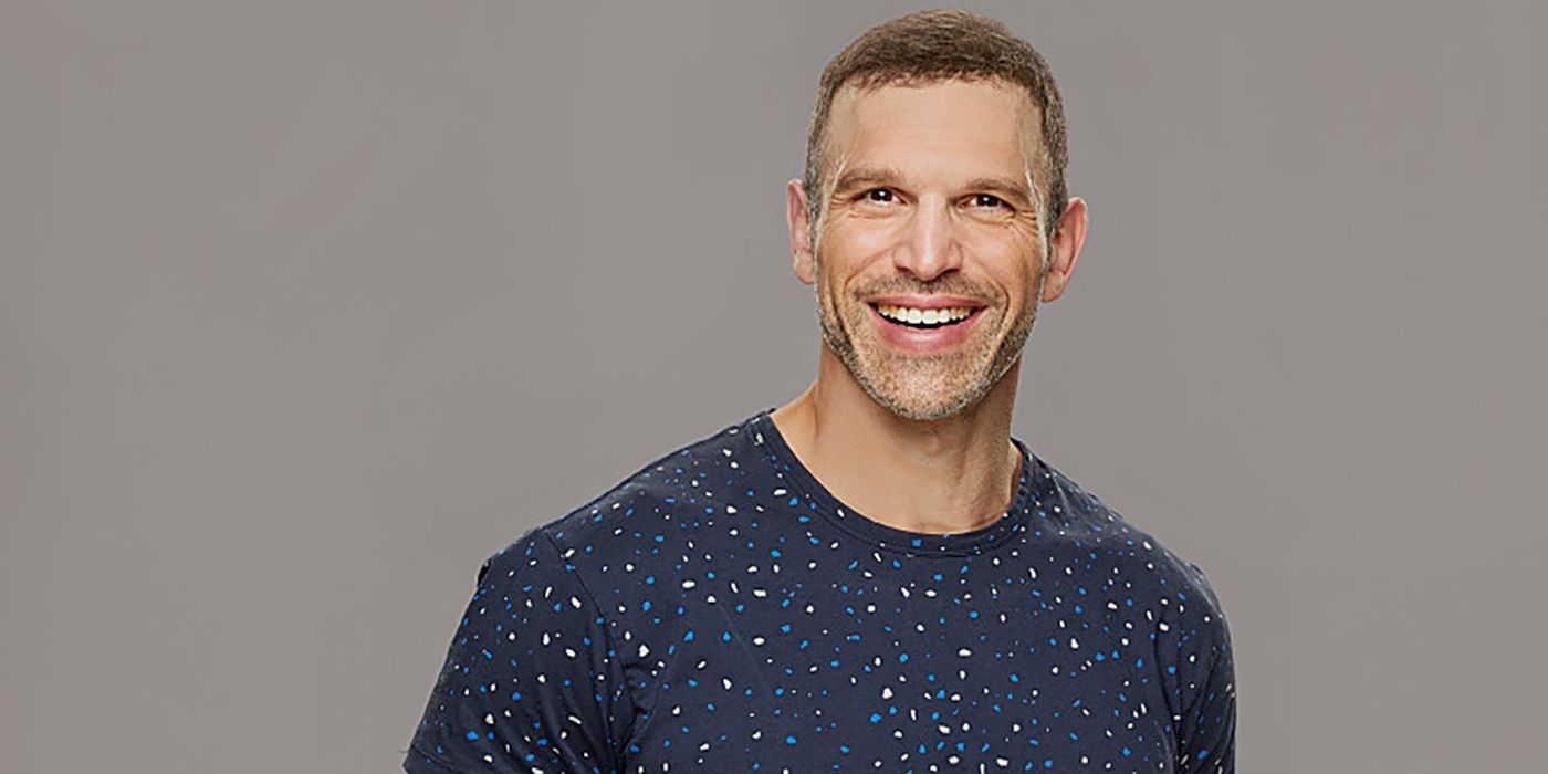 Hisam Goueli from Big Brother 25 wearing dark shirt and smiling against gray background